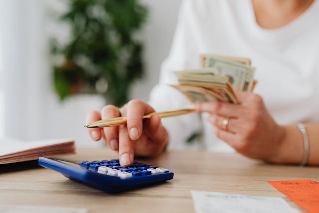 person%20holding%20cash%20while%20putting%20numbers%20into%20a%20calculator